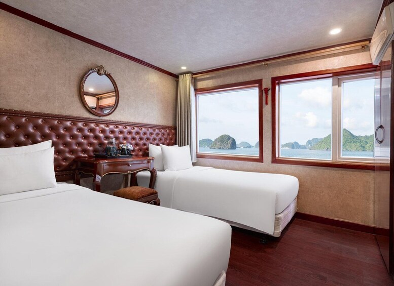 A hotel room with two beds, a wooden headboard, a desk with a mirror, and large windows overlooking the sea. 2