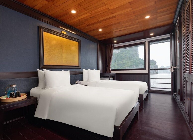 A hotel room with two beds, wooden ceiling, a large window, and a painting on the wall. 3