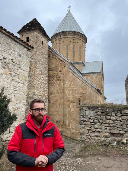 A man standing in front of a historic stone building with a tower. 2