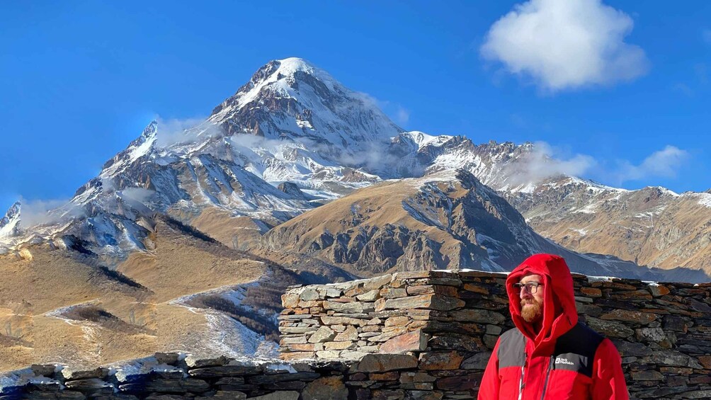 A person standing in front of a snow-covered mountain with a stone wall. 4