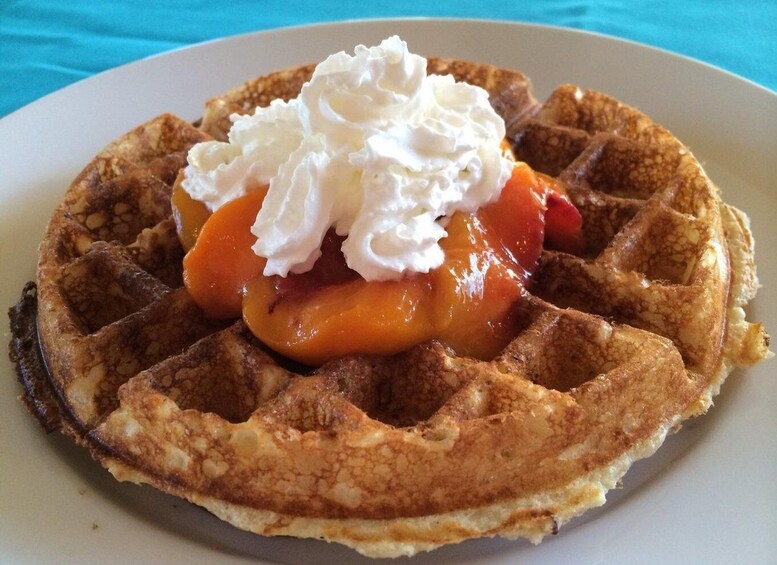 A waffle with peach slices and whipped cream on a plate. 2