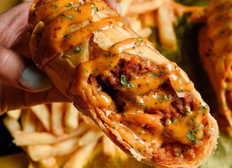 A hand holding a stuffed pastry with a visible filling, garnished with herbs. 3