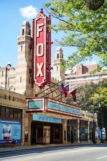 A theater with a prominent red marquee reading 'FOX' and a sign indicating 'CHAPTER ONE: A GUT PUNCHING, BREATHING, KNOCKOUT OF A MUSICAL.' 5