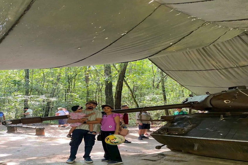 A group of people standing under a tent with a large tank in the background. 3
