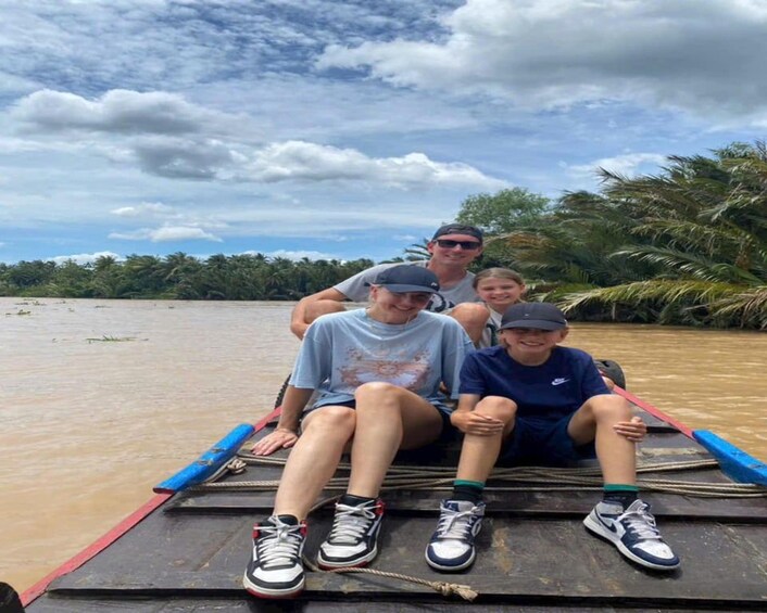 A group of people on a boat with a river and palm trees in the background. 1