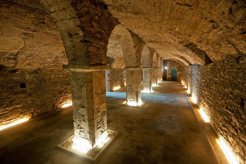 An underground passage with stone columns and arches, illuminated by artificial lighting. 4