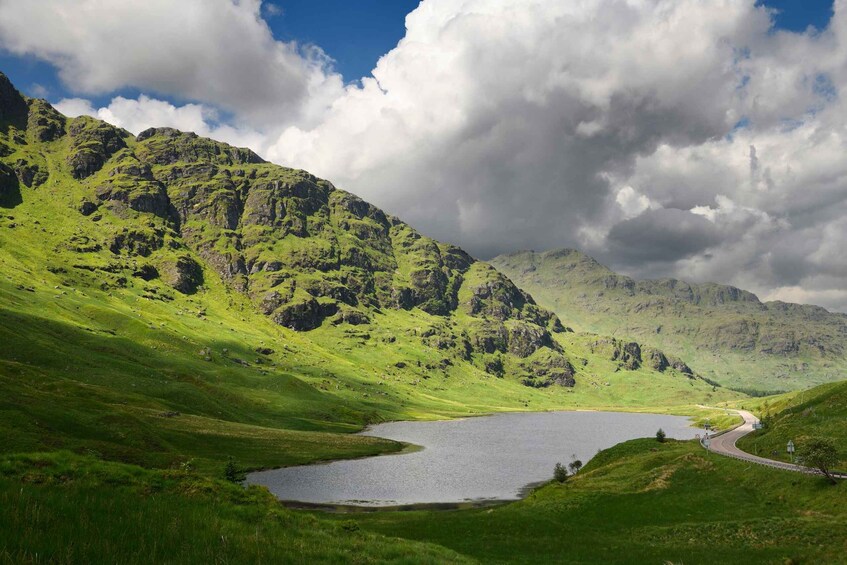 A lake surrounded by green hills and mountains under a partly cloudy sky. 3