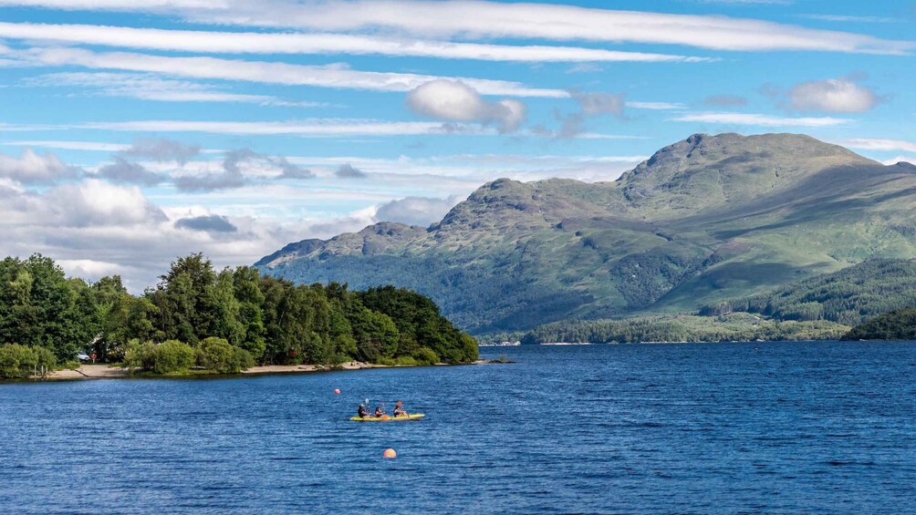 A lake with kayakers, a forested island, and mountains in the background. 1