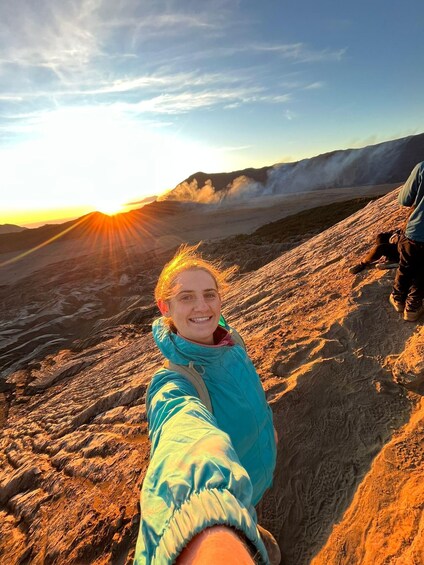 A person taking a selfie on a rocky terrain with a sunset in the background. 3