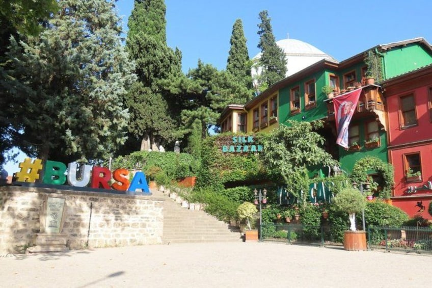 A sign with colorful letters spelling 'BURSA' and a building with a green facade in the background. 4
