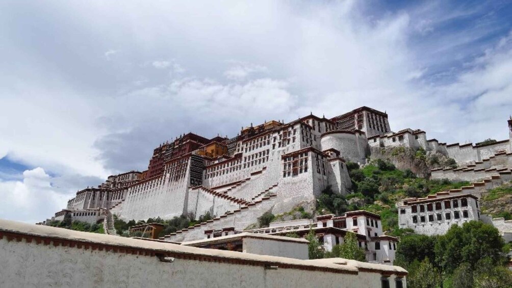 A large, multi-tiered monastery complex with a prominent central building, surrounded by smaller structures and set against a cloudy sky. 4
