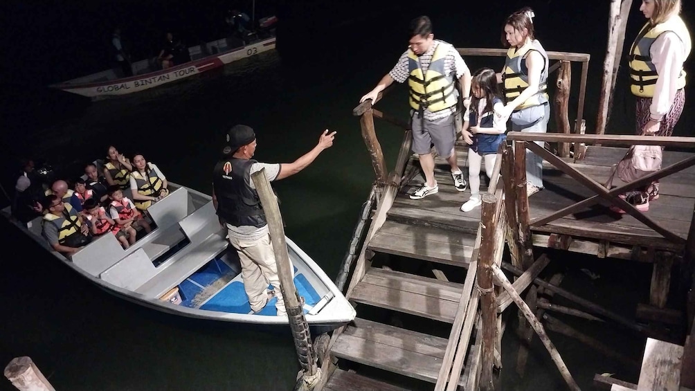 A boat tour with passengers wearing life jackets, a guide leading the boat, and a dock with wooden stairs. 3