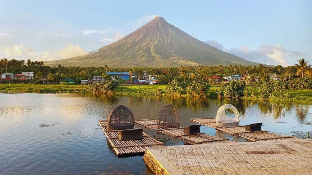A calm lake with wooden platforms and birdhouses, a mountain in the background, and a small village with houses and palm trees. 5