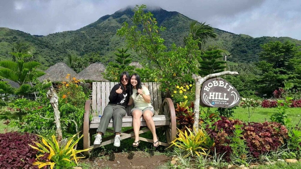 Two people sitting on a wooden bench with a sign reading 'Hobbit Hill' in the background. 4
