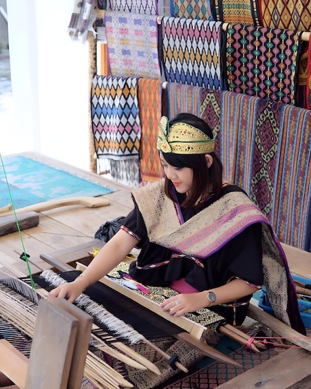 A person weaving on a loom with colorful textiles in the background. 2