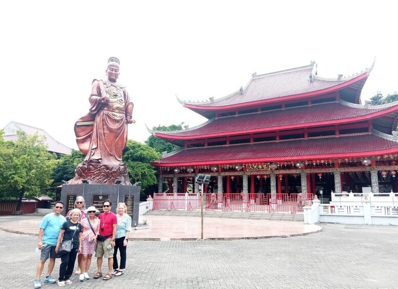 A large bronze statue of a woman in traditional attire, a red pagoda-style building, and a group of people posing in front. 2