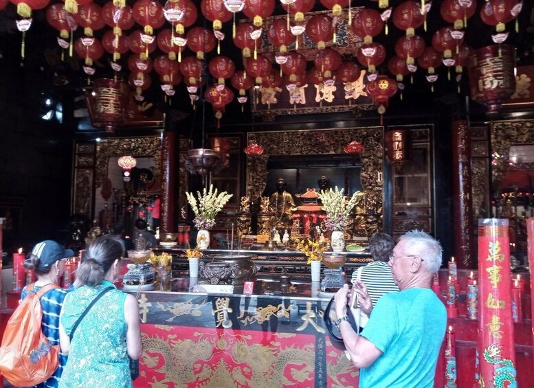 A temple interior with red lanterns, statues, and incense burners. 1