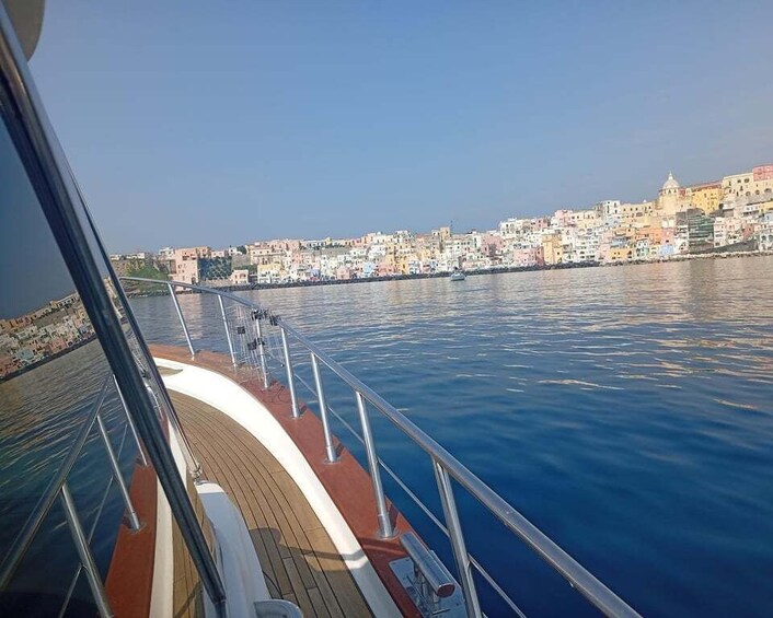 A boat deck with a railing, water, and a cityscape in the background. 2