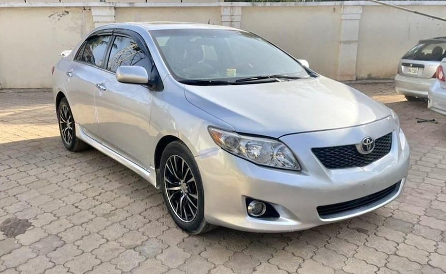 A silver Toyota sedan parked on a paved surface with a concrete wall in the background. 3