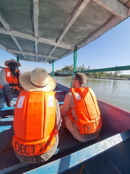 People on a boat wearing orange life jackets, with a hat on one person's head. 3
