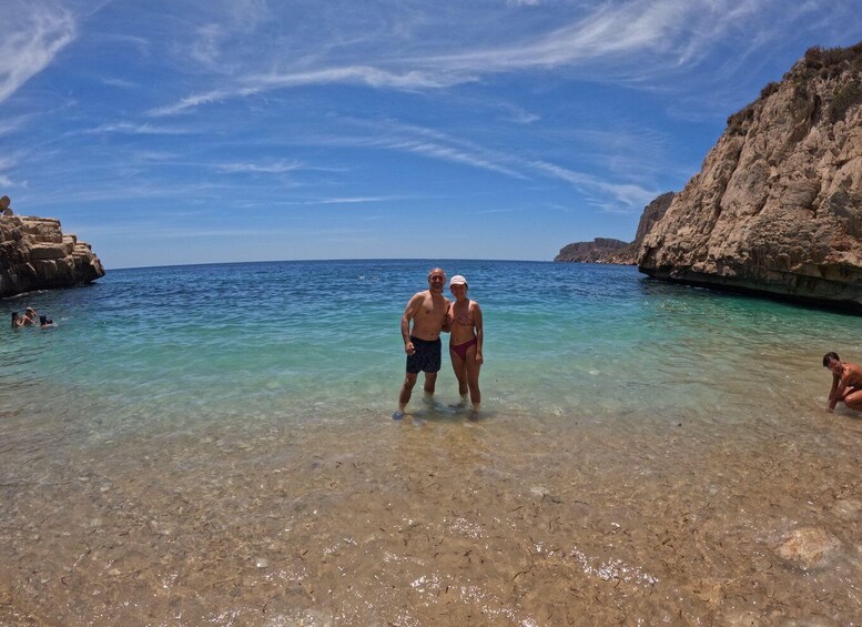 A couple standing in shallow water at a rocky coastal area with clear skies. 2