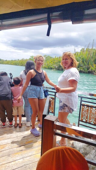 A group of people on a wooden dock by a body of water with greenery in the background. 2