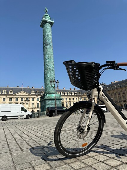 A bicycle with a basket parked on a paved area with a tall, green monument in the background. 5