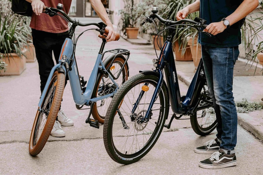 Two bicycles parked on a paved surface with potted plants in the background. 1