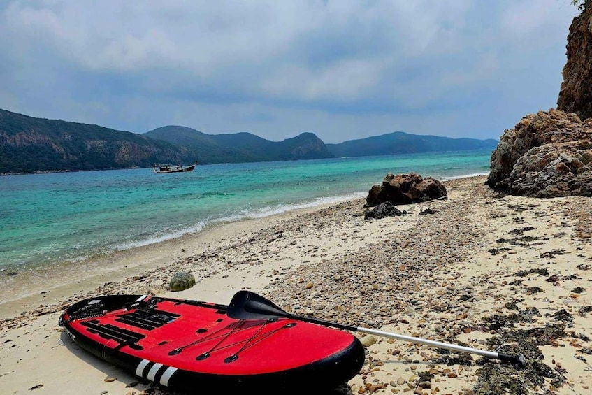 A red kayak on a pebble beach with a clear turquoise sea and distant mountains. 3