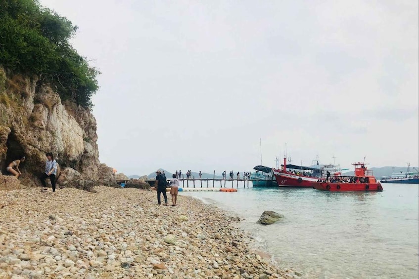 A pebbled beach with people, a rocky cliff, and a red boat docked at a pier. 4