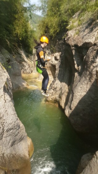 A person in a black wetsuit and yellow helmet jumping into a river. 5