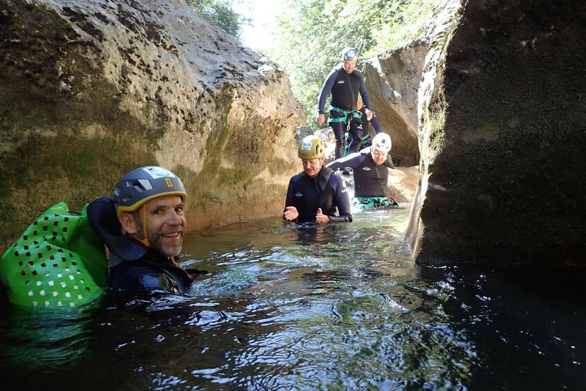 People in water with helmets, wearing life jackets, and climbing a rocky wall. 2