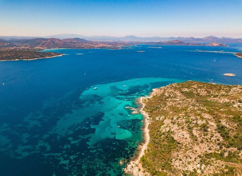 An aerial view of a coastal area with clear blue waters, a sandy beach, and a hilly landscape. 5