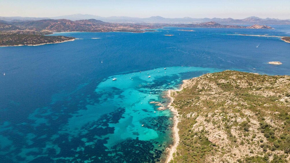 A coastal landscape with clear blue waters, a sandy beach, and a hilly terrain. 2