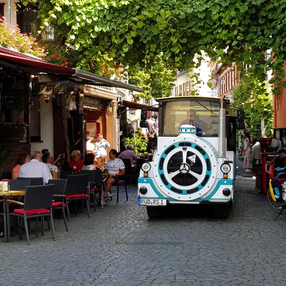 A vintage car parked on a cobblestone street, surrounded by cafes and pedestrians. 3