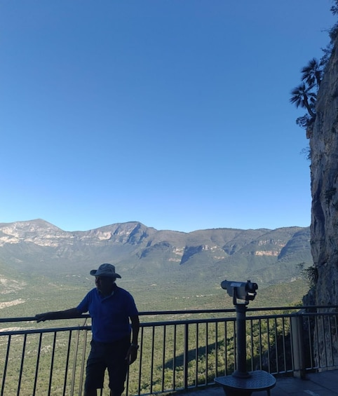 A person standing on a balcony with a telescope, overlooking a mountainous landscape. 2