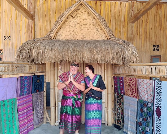 A traditional wooden structure with a thatched roof, surrounded by colorful woven textiles. 1