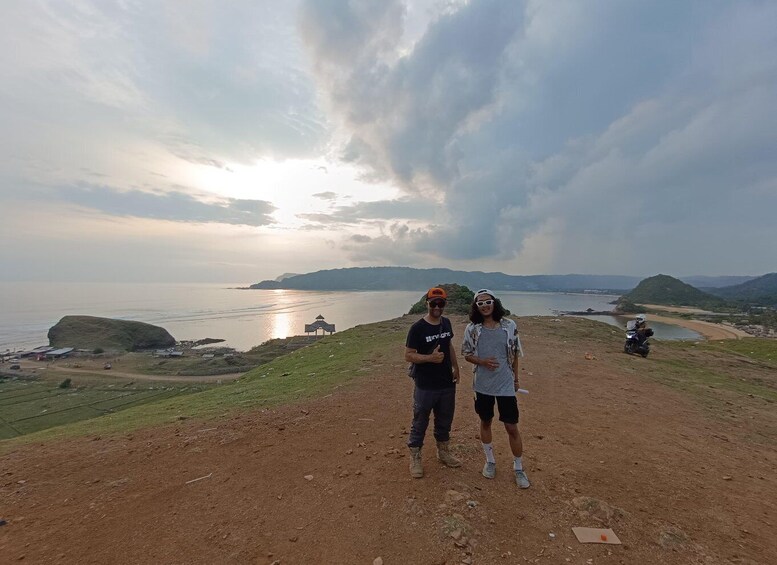 Two people standing on a dirt path with a coastal landscape in the background. 2