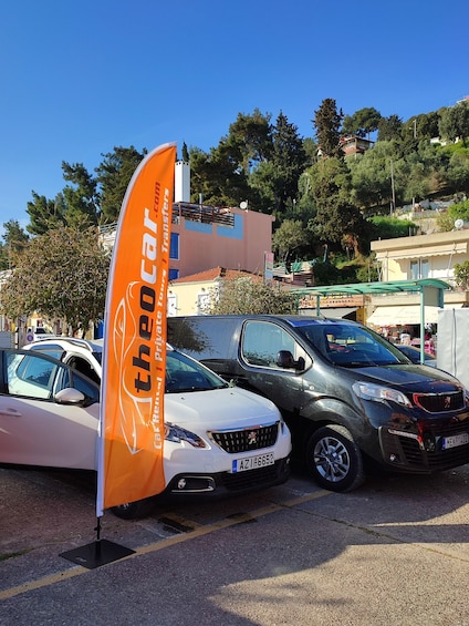 A parking area with several cars, a prominent orange flag, and buildings in the background. 2