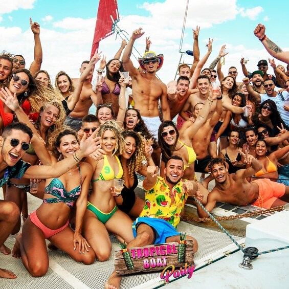A group of people on a boat, some wearing swimsuits, with a sign that reads 'Tropical Boat Party'. 5