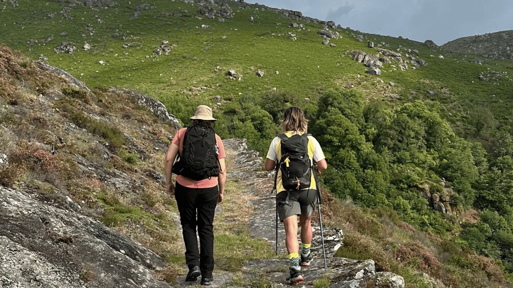 Two hikers on a rocky trail with green hills in the background. 4
