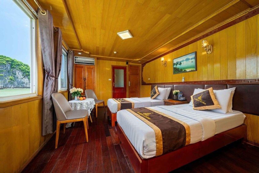 A cabin with wooden walls and floors, two beds with matching headboards, a small table with a vase of flowers, and a window with curtains. 4