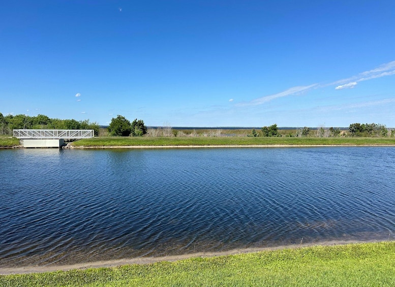 A calm lake with a white bridge, grassy banks, and trees in the background. 2