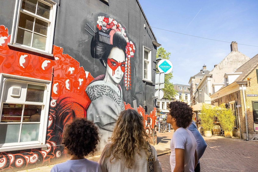 A street with a mural of a woman in traditional attire, a sign for 'KAHUNA', and a cobblestone street. 1