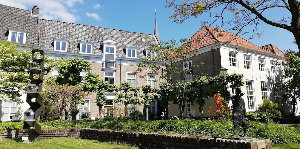 A row of traditional European buildings with a mix of brick and white facades, surrounded by lush greenery and a clear blue sky. 2