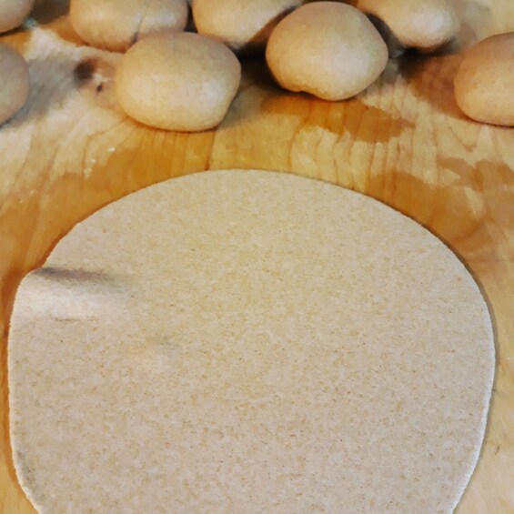 A round flatbread on a wooden surface with several round bread rolls in the background. 3