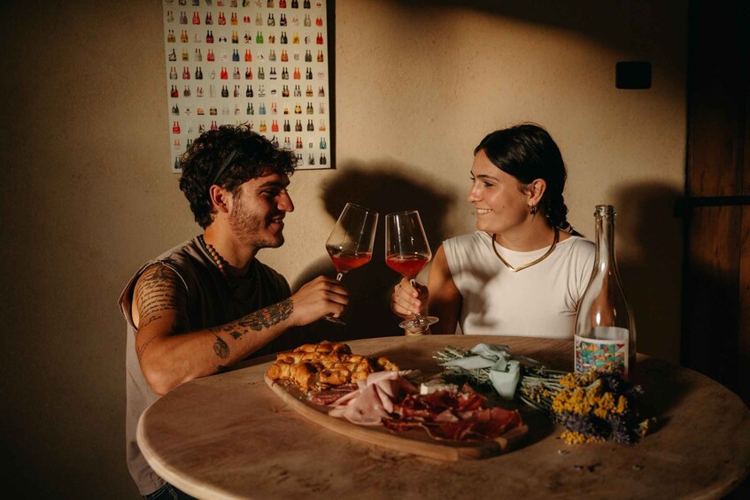Two people toasting with wine glasses at a table with food and a bottle. 5