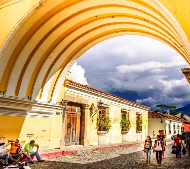 A street scene with a yellow building, a stone archway, and a cloudy sky. 4