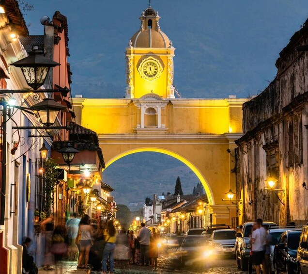 A historic street with a prominent archway, a clock tower, and illuminated street lamps. 3