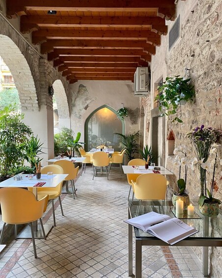 An outdoor cafe with yellow chairs and tables, surrounded by plants and a stone wall. 5